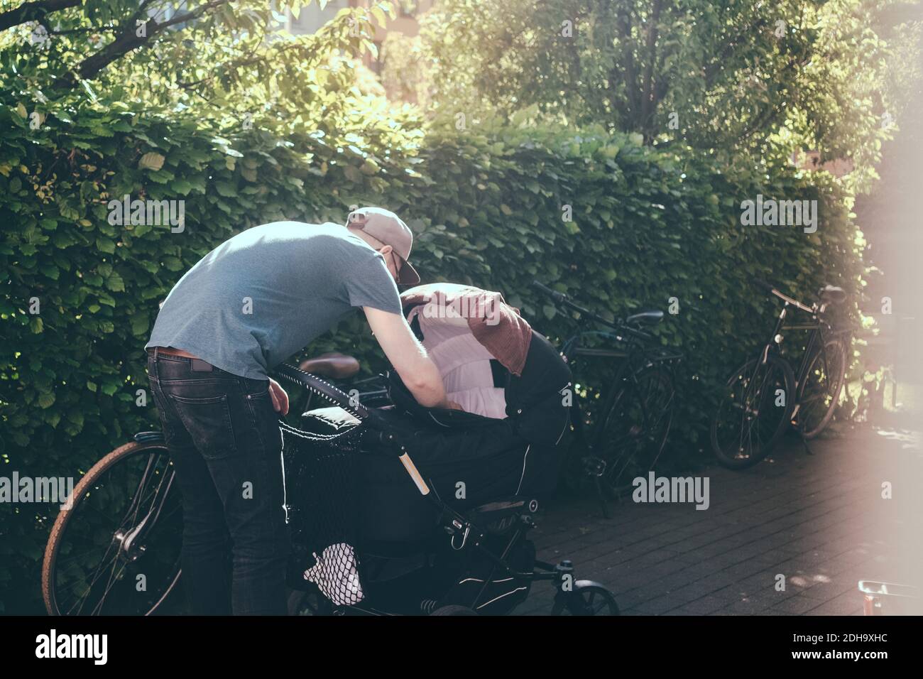 Full length of father bending over baby carriage on footpath at park during sunny day Stock Photo