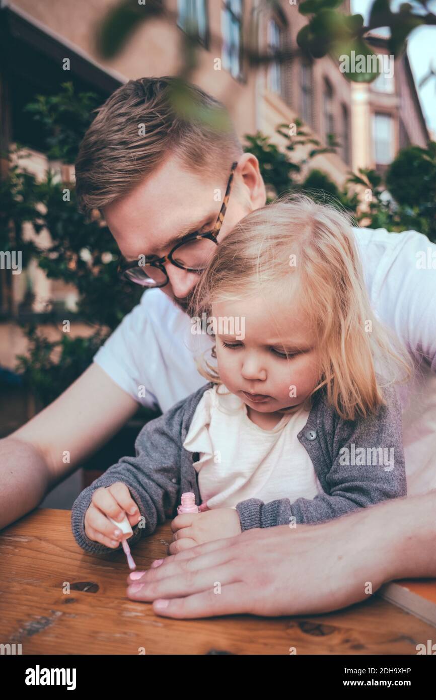 Daughter painting father's fingernails at table outdoors Stock Photo