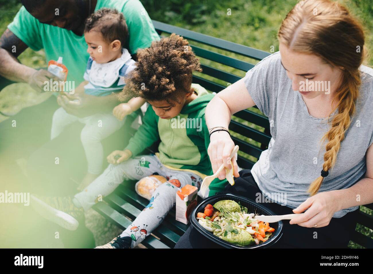 High angle view of family having food while sitting on bench at park ...