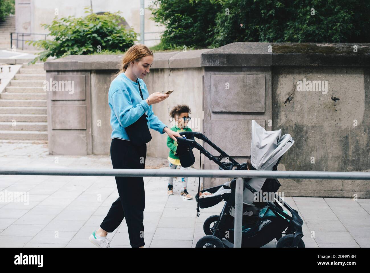 Mother with son using mobile phone while pushing baby stroller on ...