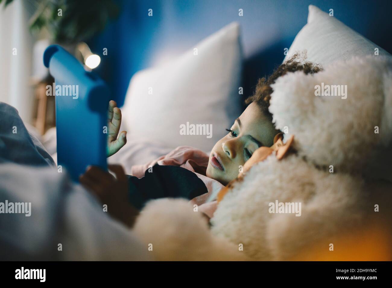 Boy lying with teddy bear while using digital tablet on bed at home Stock Photo
