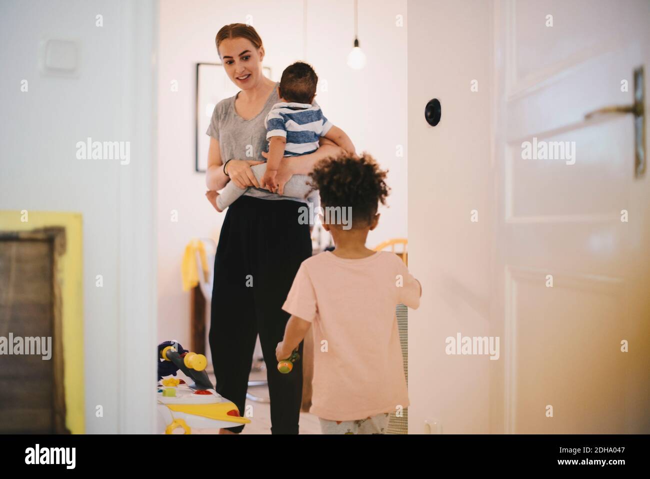 Mother carrying toddler looking at son while standing in domestic room Stock Photo