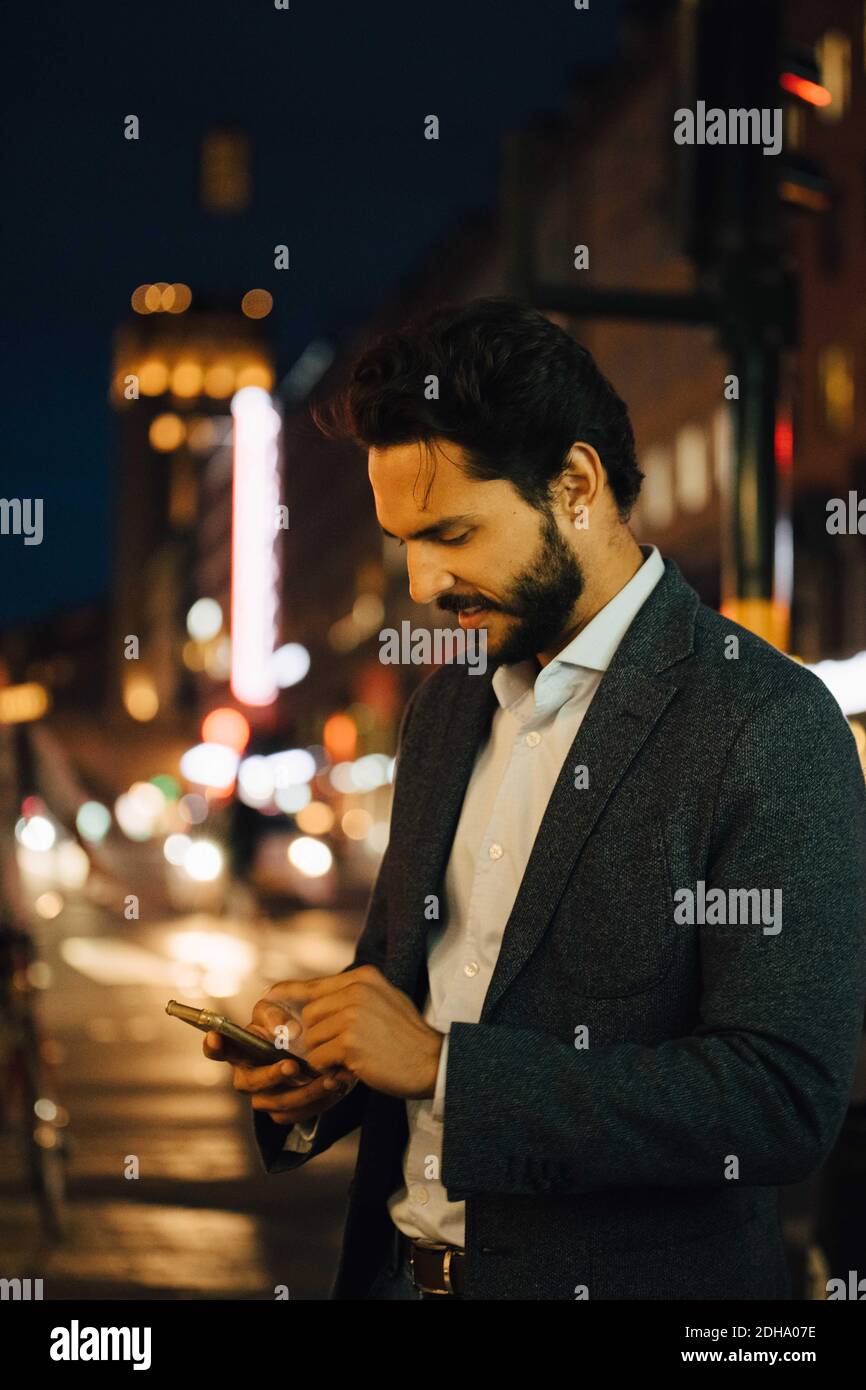 Man using smart phone while standing in city at night Stock Photo