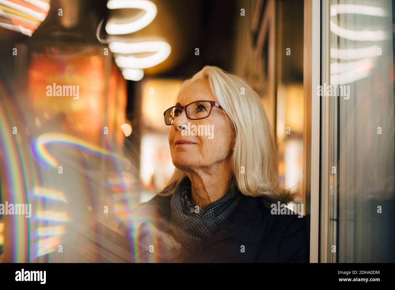 Wrinkled smiling woman looking up while standing in illuminated city at night Stock Photo