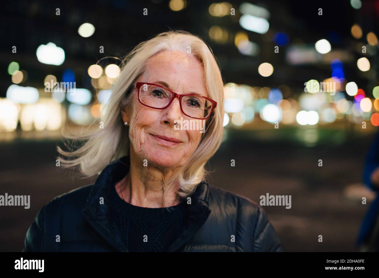 Portrait of wrinkled smiling woman standing in illuminated city at night Stock Photo