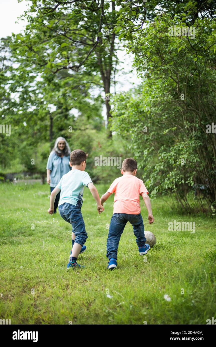 Grandmother looking at twin boys playing soccer in back yard Stock Photo