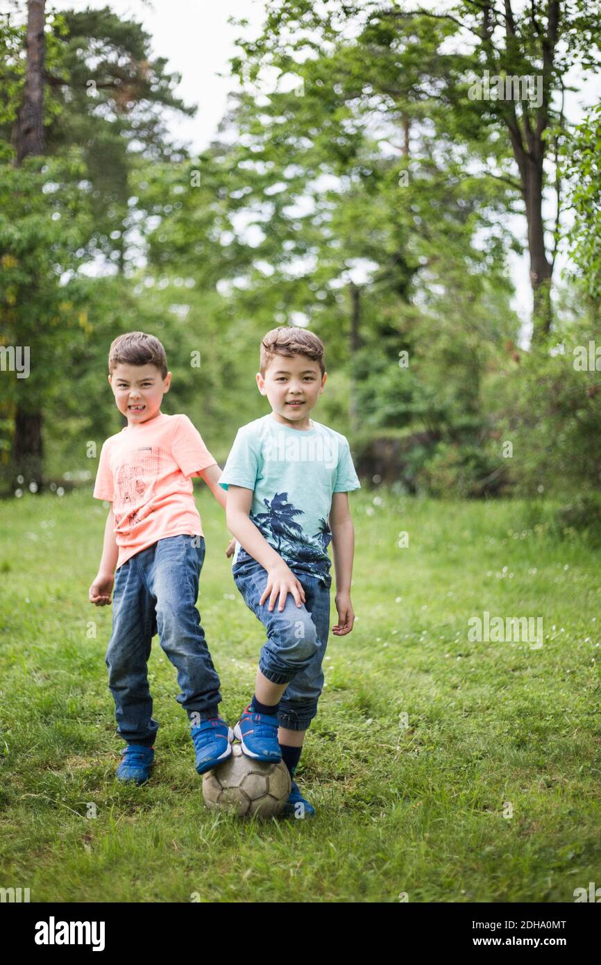 Portrait of twin boys standing with soccer ball at back yard Stock