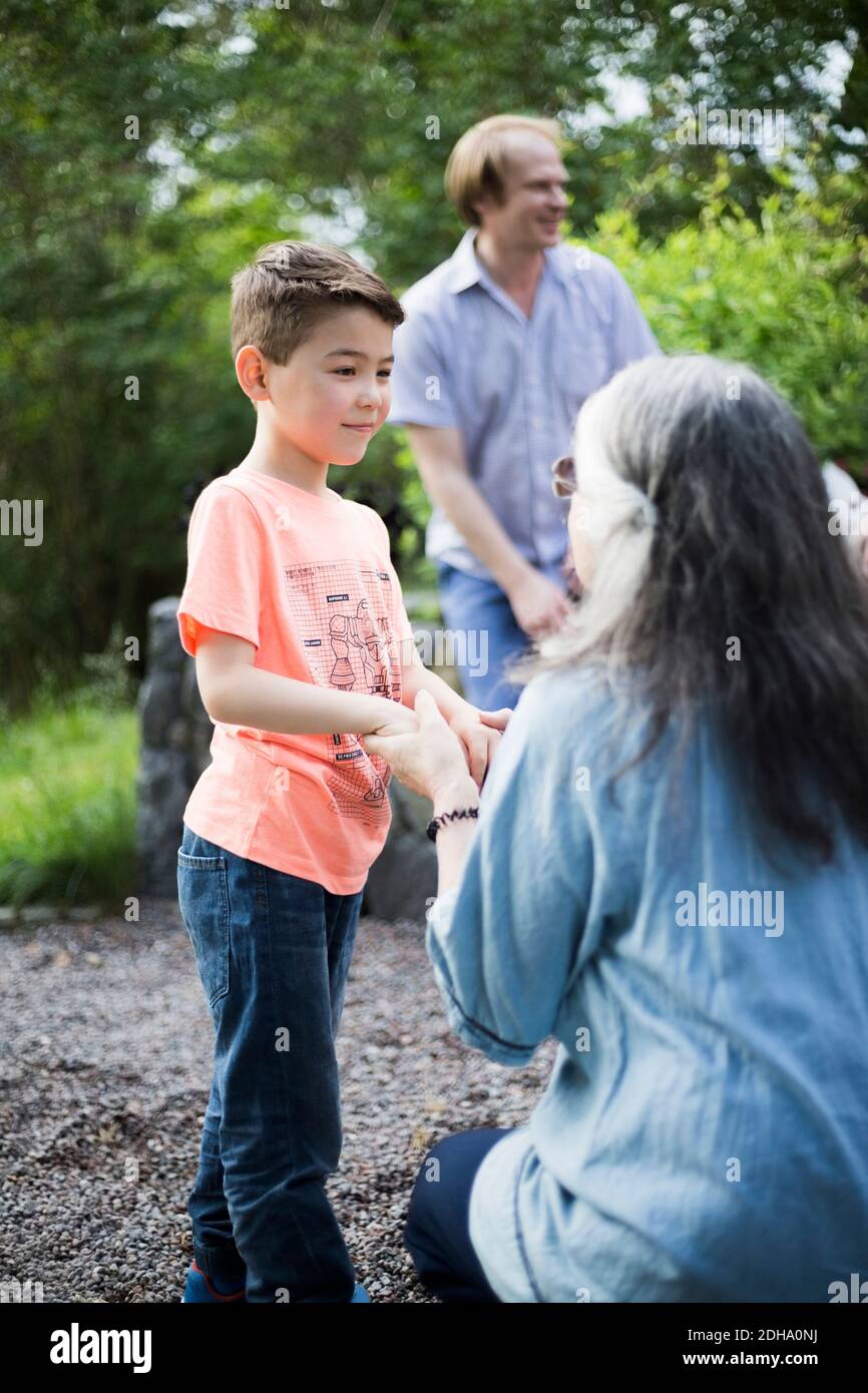 Grandmother crouching while holding hands of grandson in back yard Stock Photo