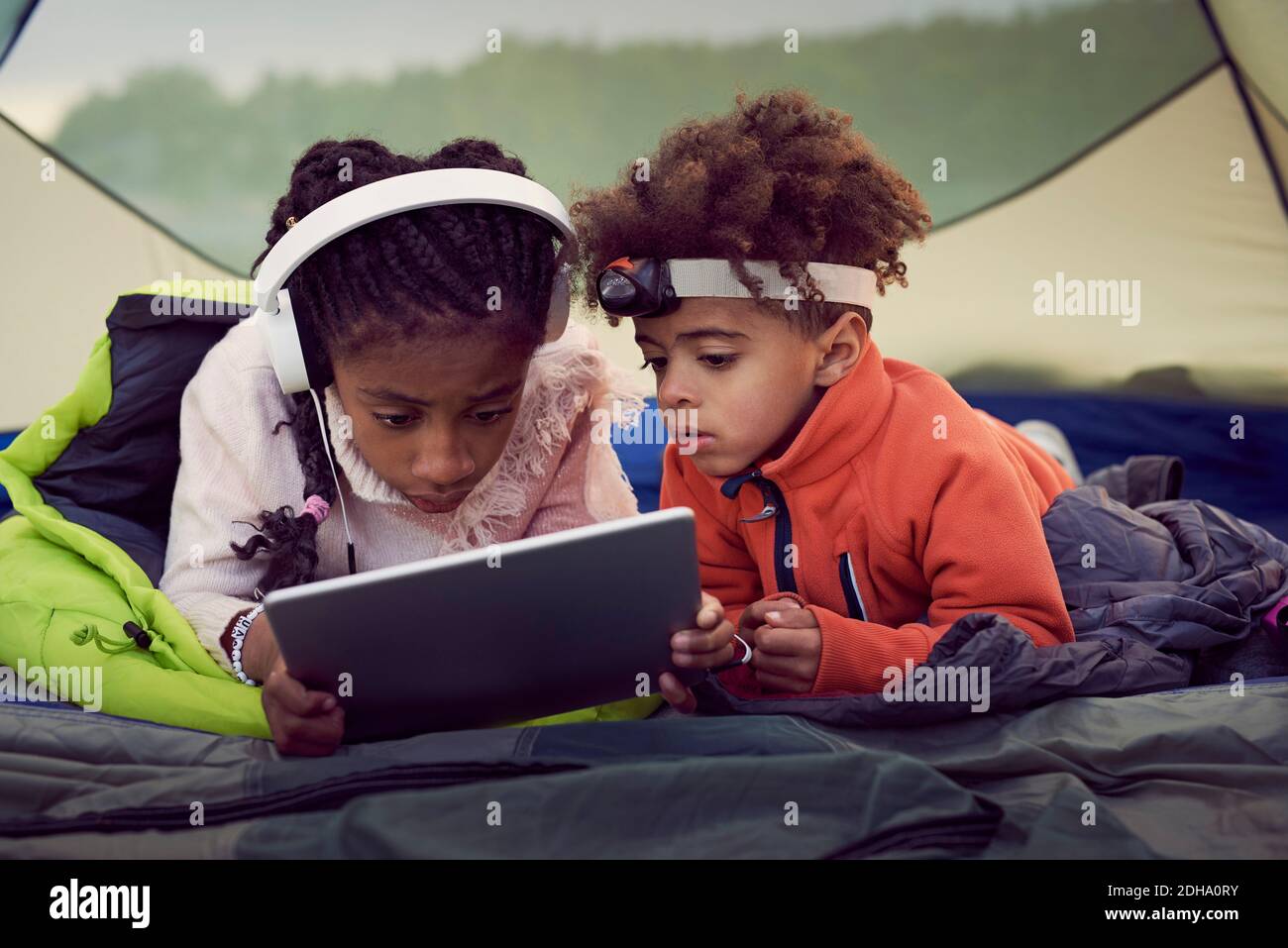 Brother and sister lying in tent while using digital tablet Stock Photo ...