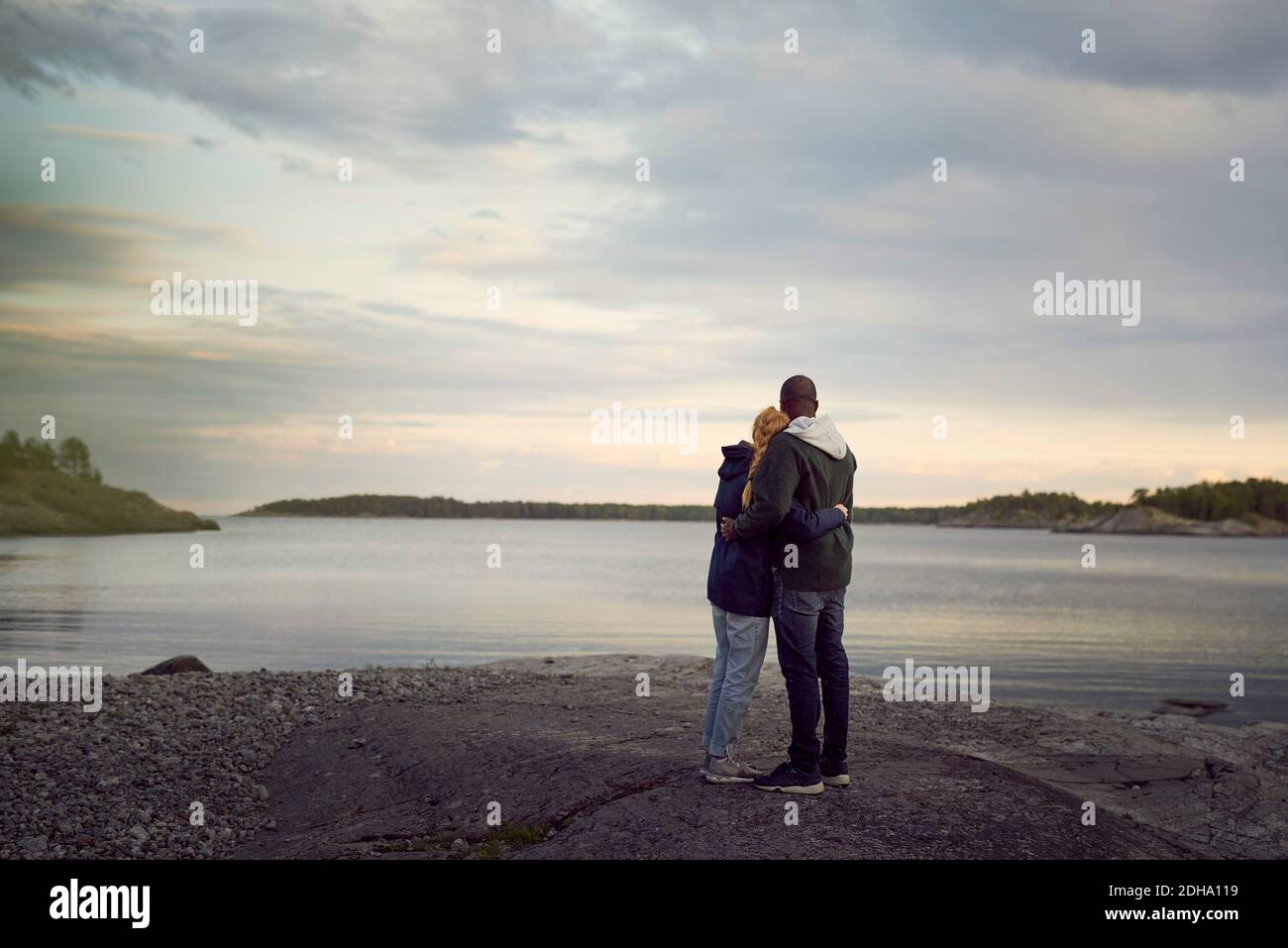 Rear view of couple standing at beach while looking at lake against sky during sunset Stock Photo