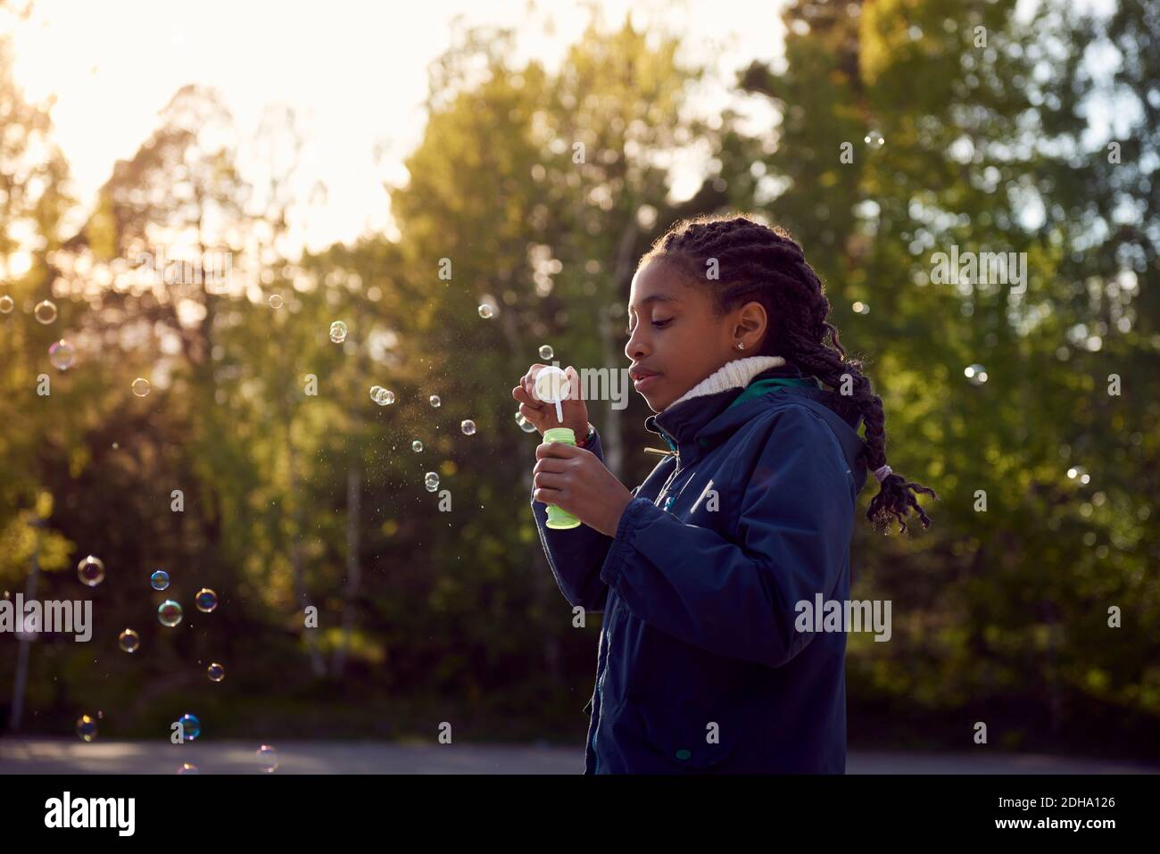 Side view of girl holding bubble wand against trees at campsite Stock Photo