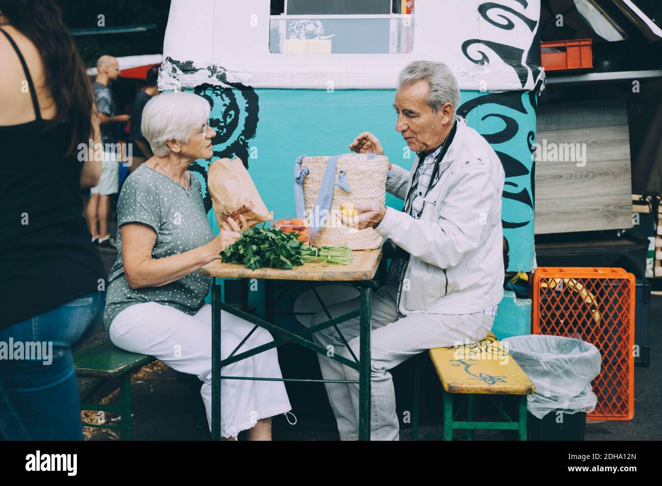 Senior man and woman discussing vegetables while sitting at market in city Stock Photo