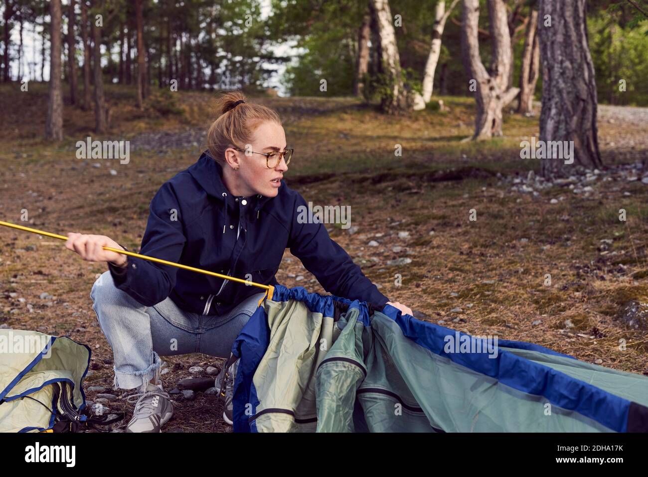Young woman crouching while setting up tent against trees at campsite Stock Photo