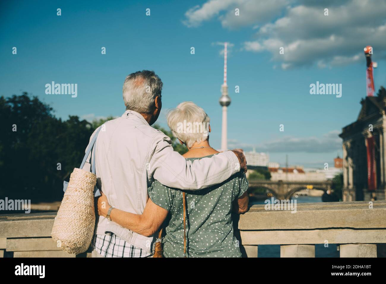 Rear view of senior couple with arm around looking at television tower from bridge in city Stock Photo