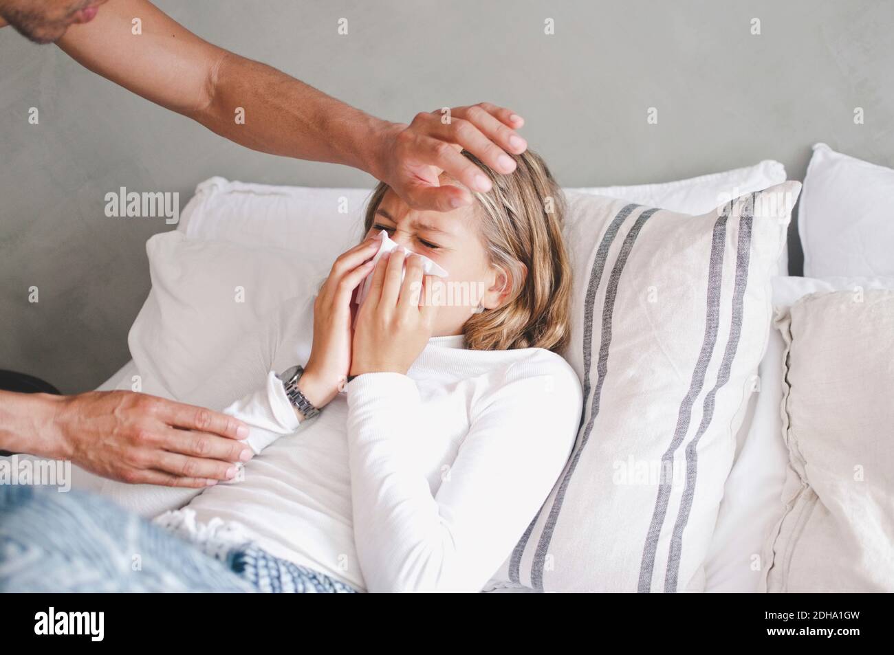 Father touching sick daughter blowing nose on bed at home Stock Photo
