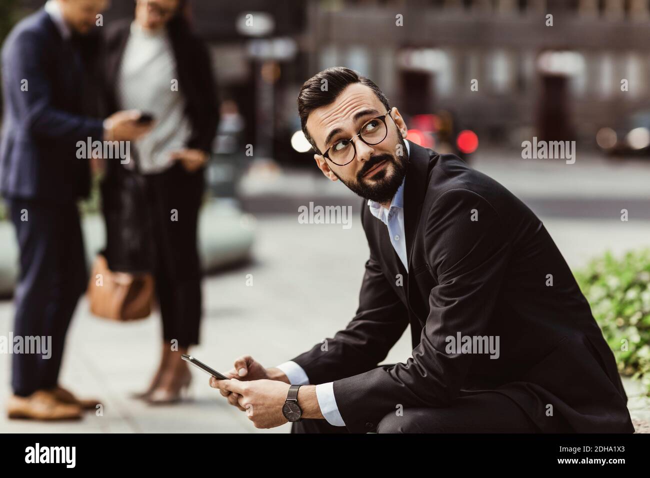 Businessman looking up while using mobile phone outdoors Stock Photo