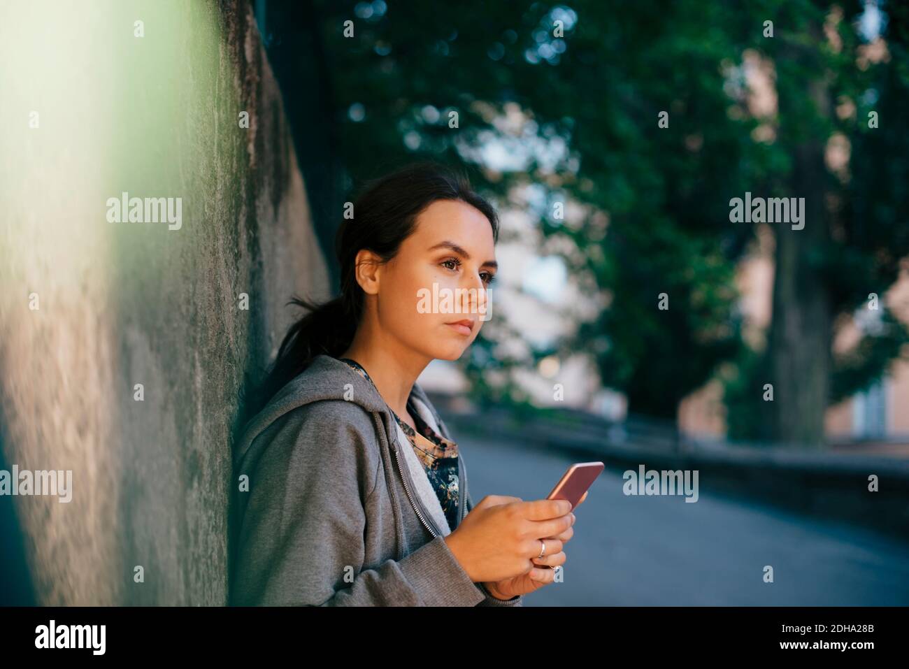 Side view of young woman holding smart phone while looking away Stock Photo