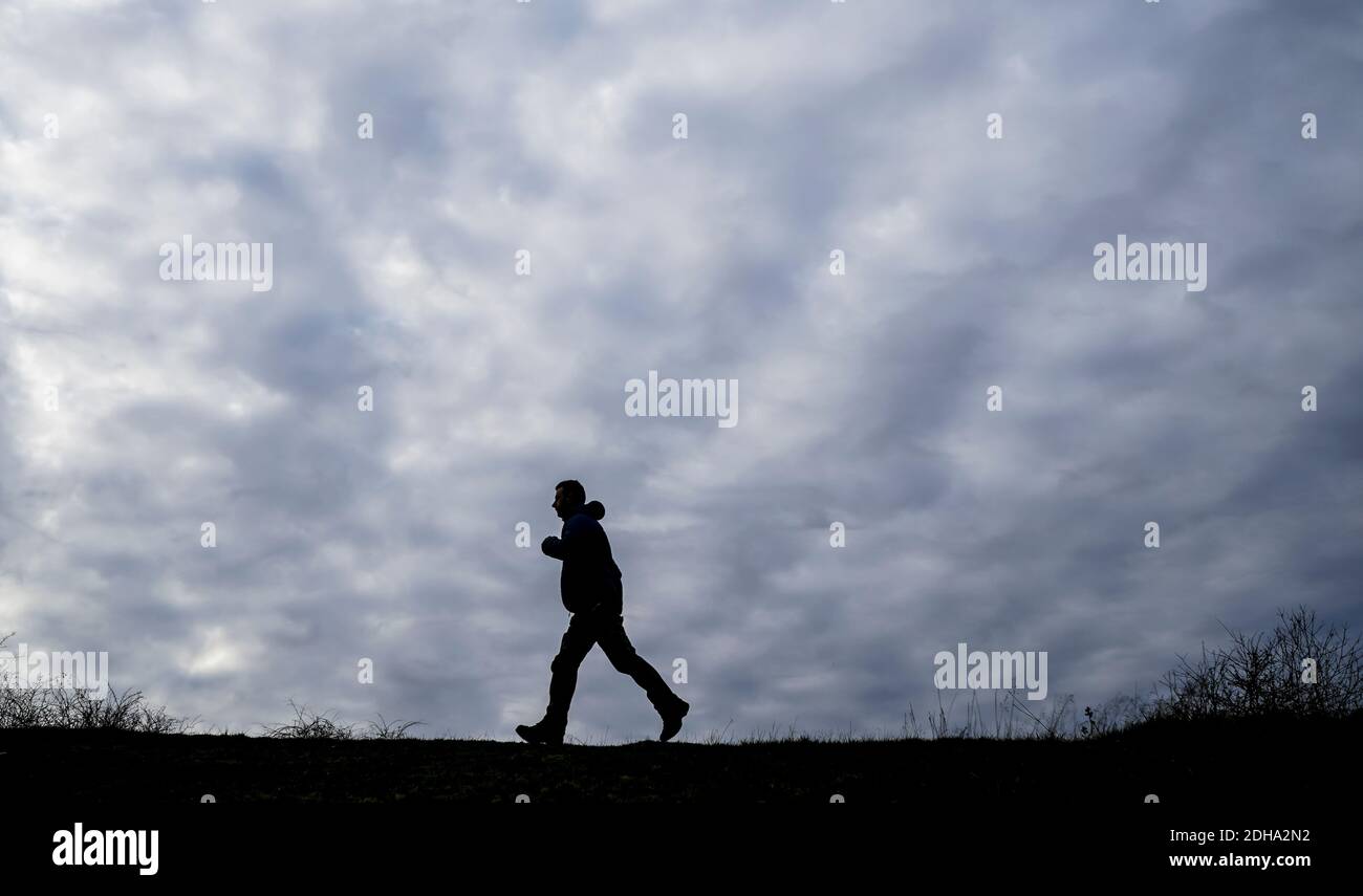 Side view silhouette of a man walking isolated outdoors in UK countryside against a dark, cloudy, winter sky background. Stock Photo