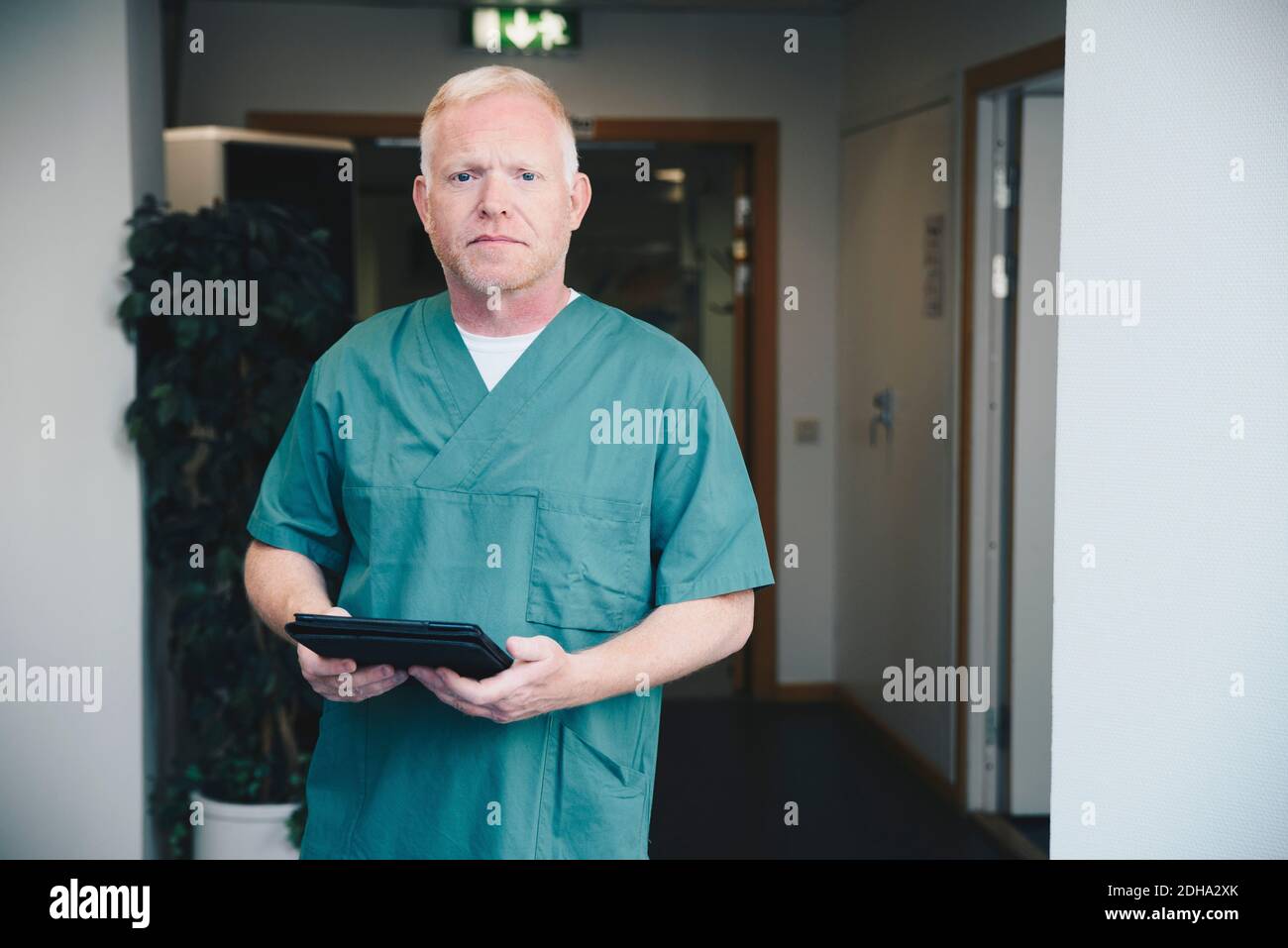 Portrait of confident mature male nurse holding digital tablet at hospital corridor Stock Photo