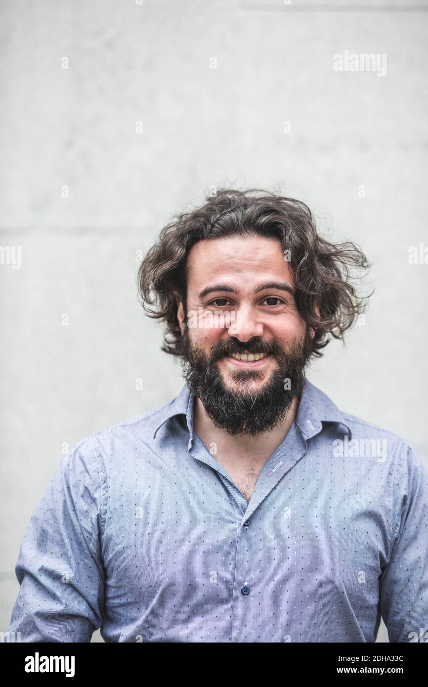Portrait of smiling businessman with beard standing against wall Stock Photo
