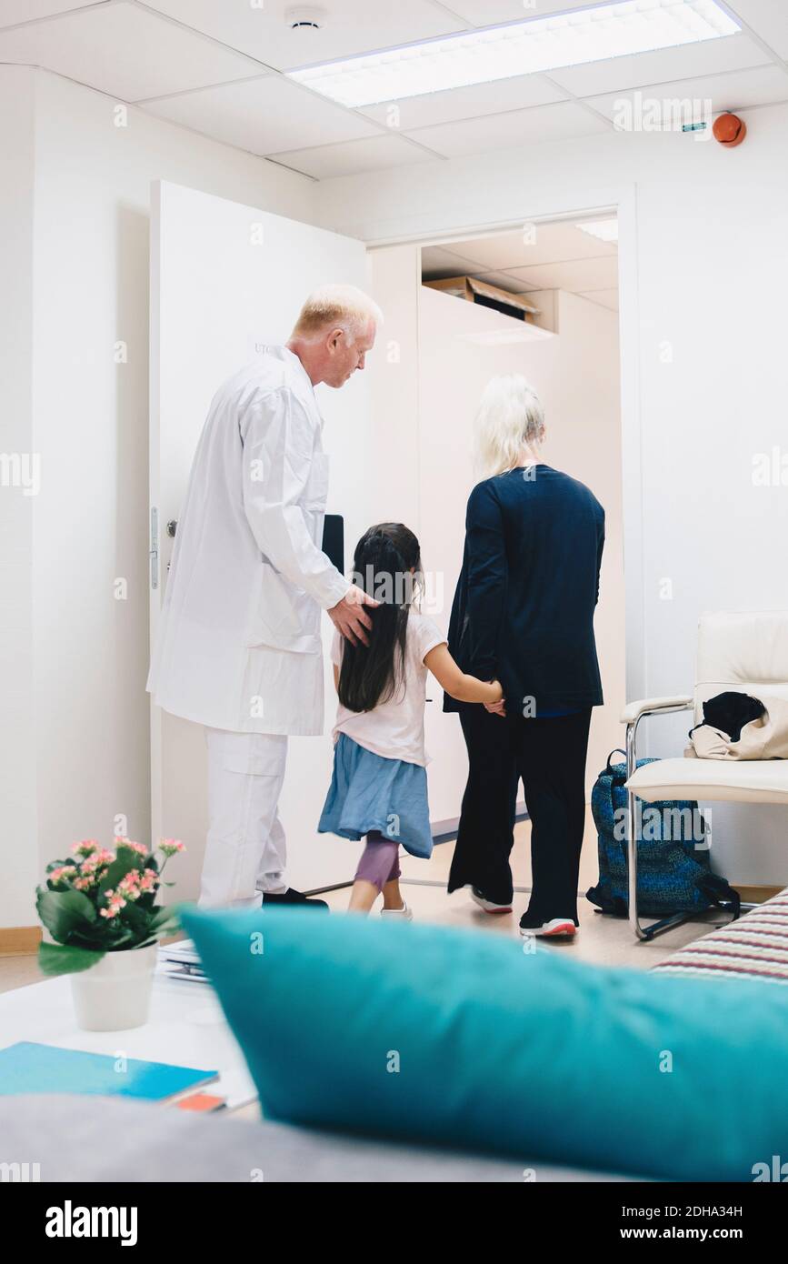 Rear view of girl walking with mother and doctor at hospital Stock ...