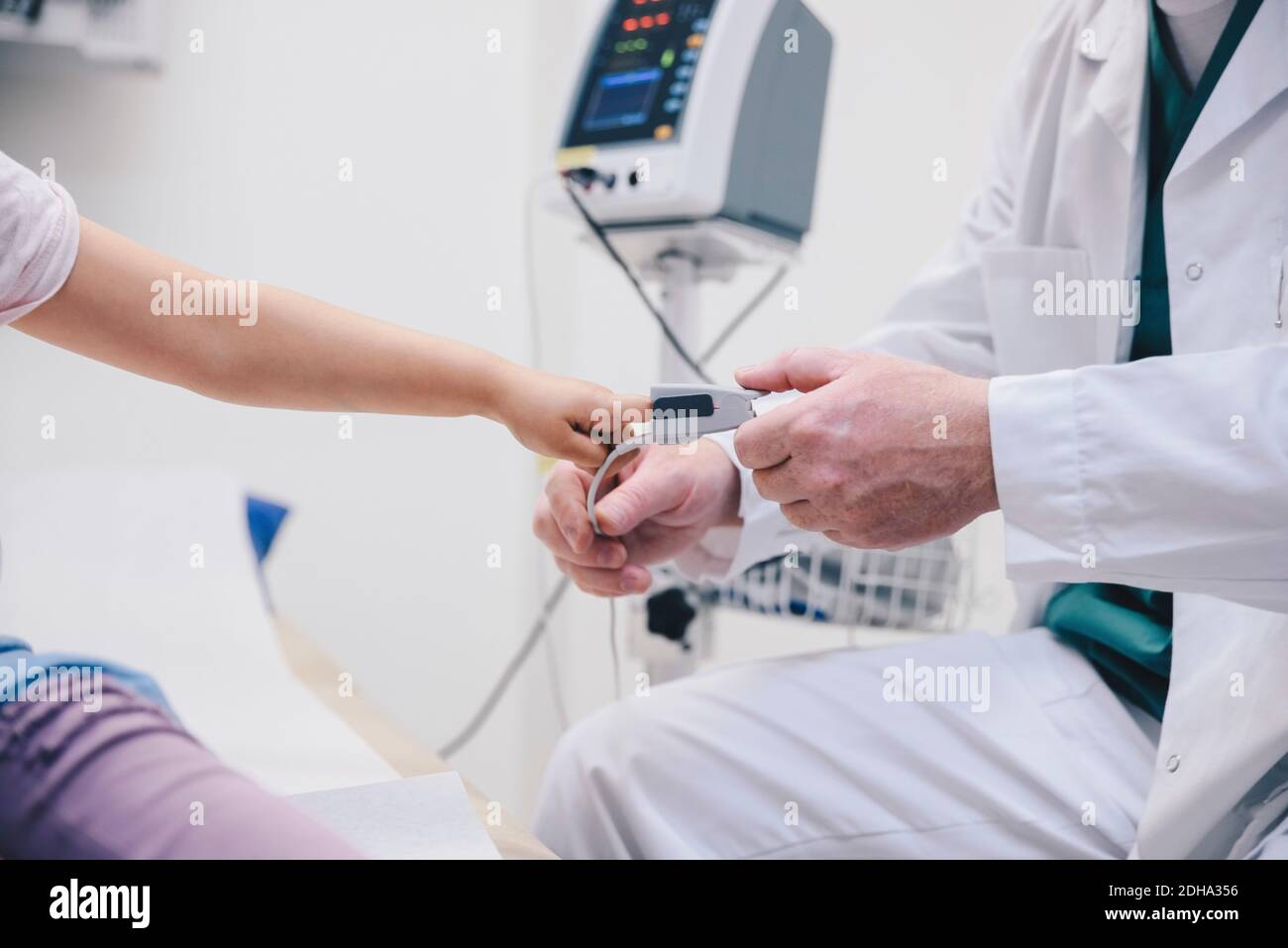 Midsection of mature doctor adjusting pulse oxymeter on girl's finger at hospital Stock Photo
