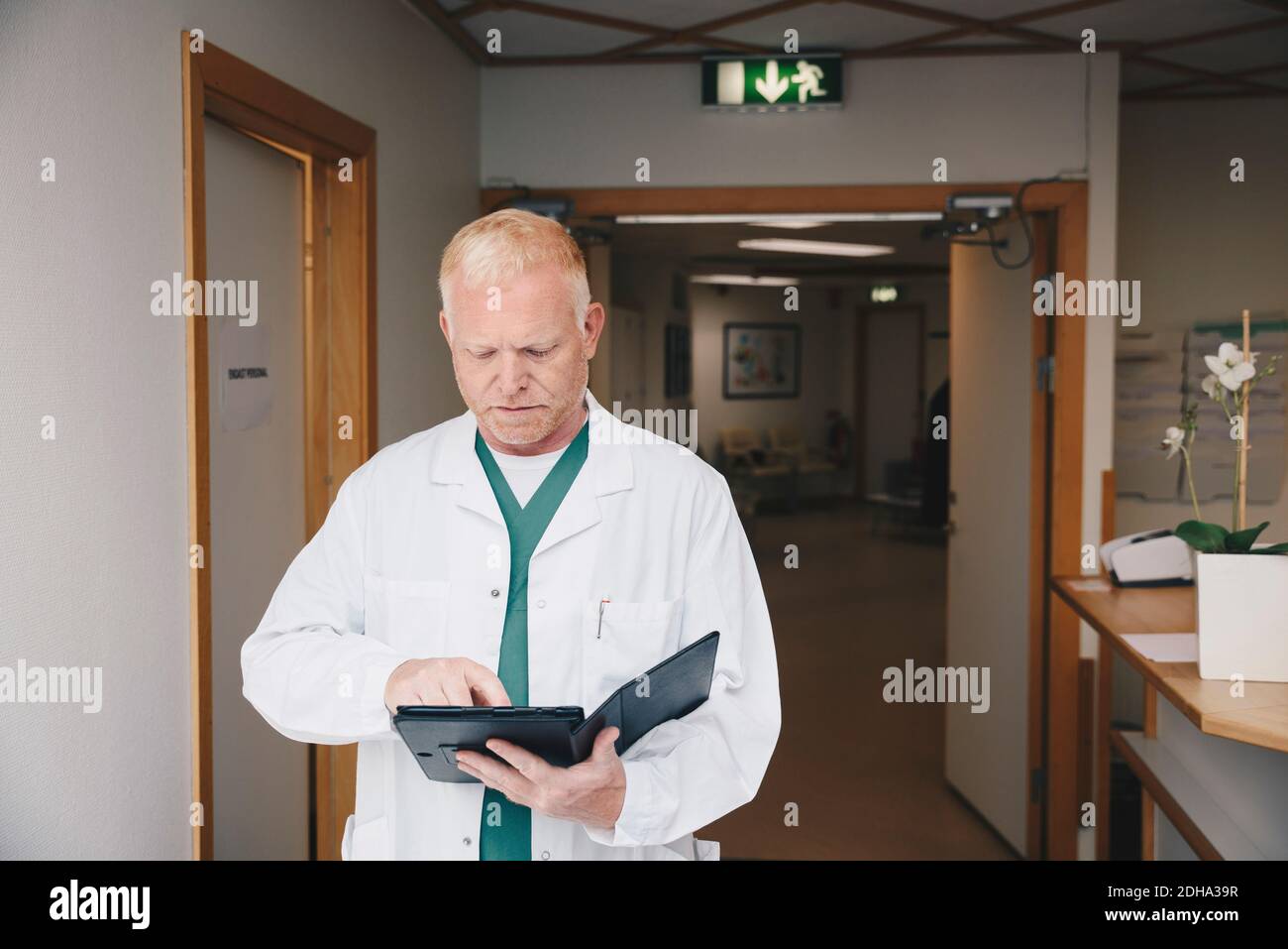Mature doctor using digital tablet while standing in hospital corridor Stock Photo