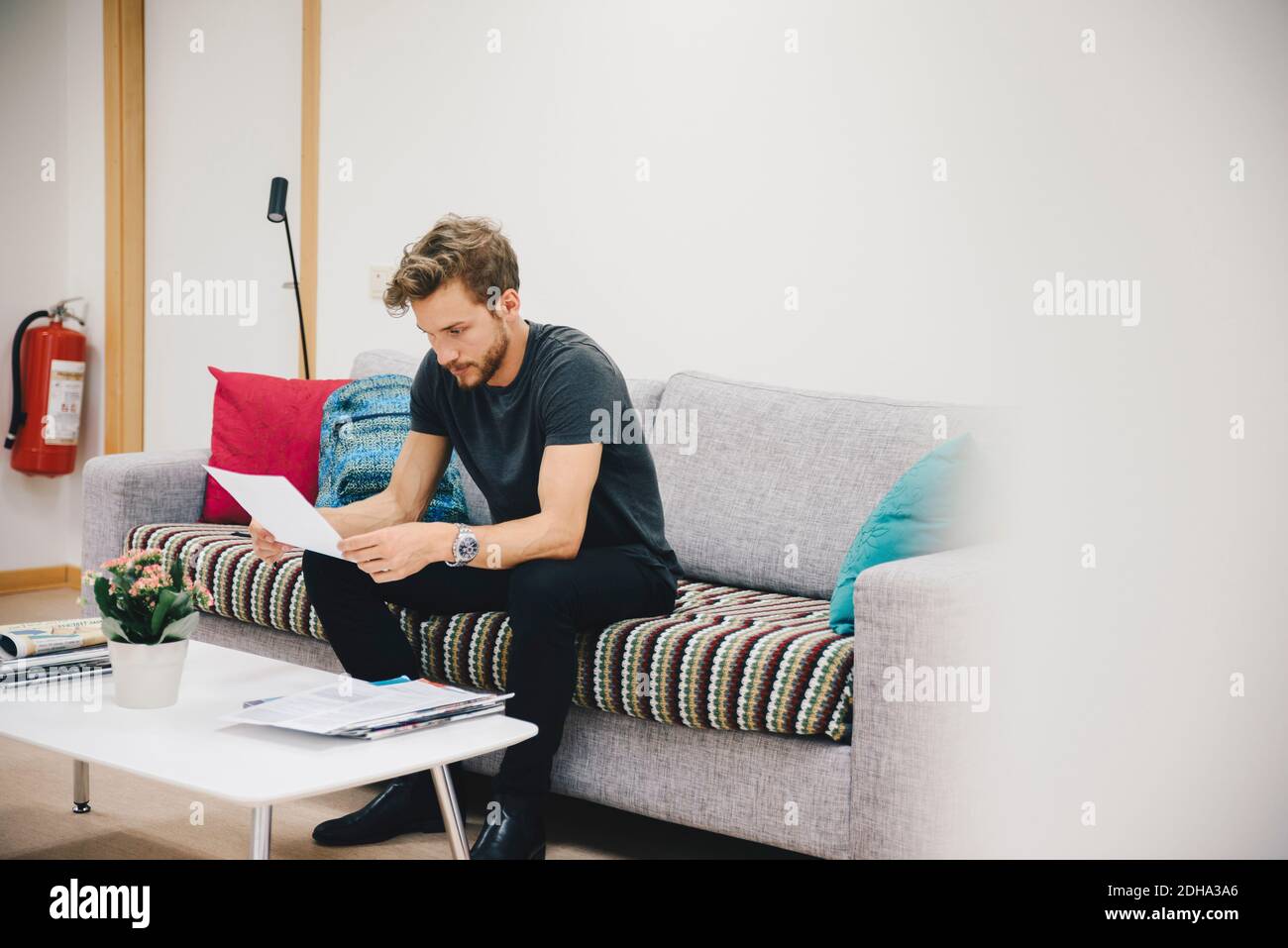 Young male patient reading document while sitting on sofa at hospital Stock Photo