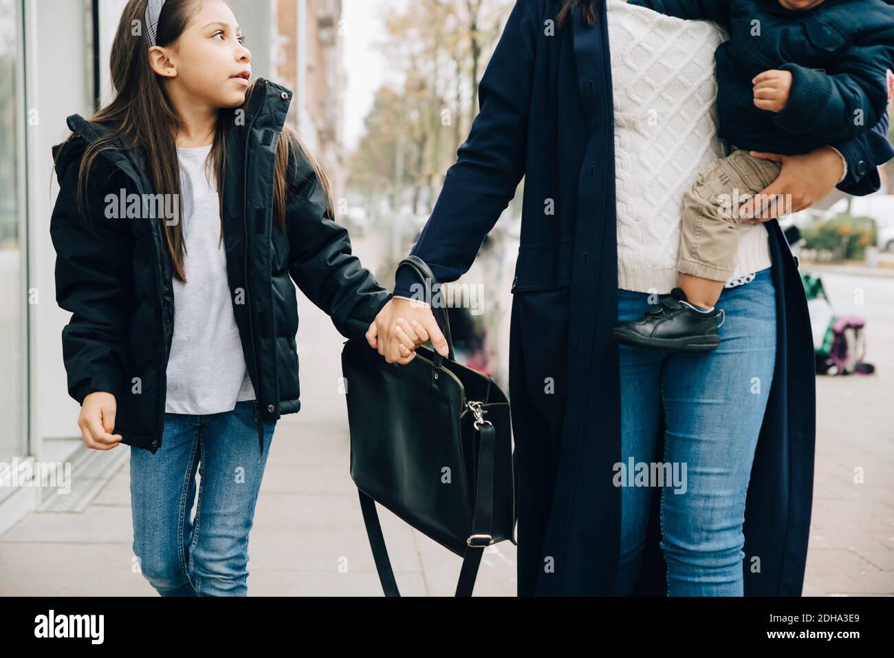 Midsection of working mother holding children walking on sidewalk in city Stock Photo