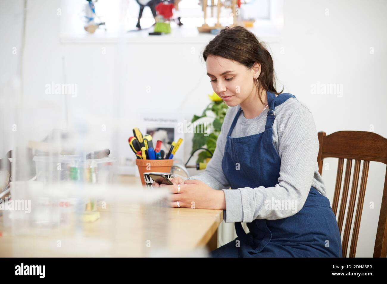 Young female engineer using smart phone at table in workshop Stock Photo
