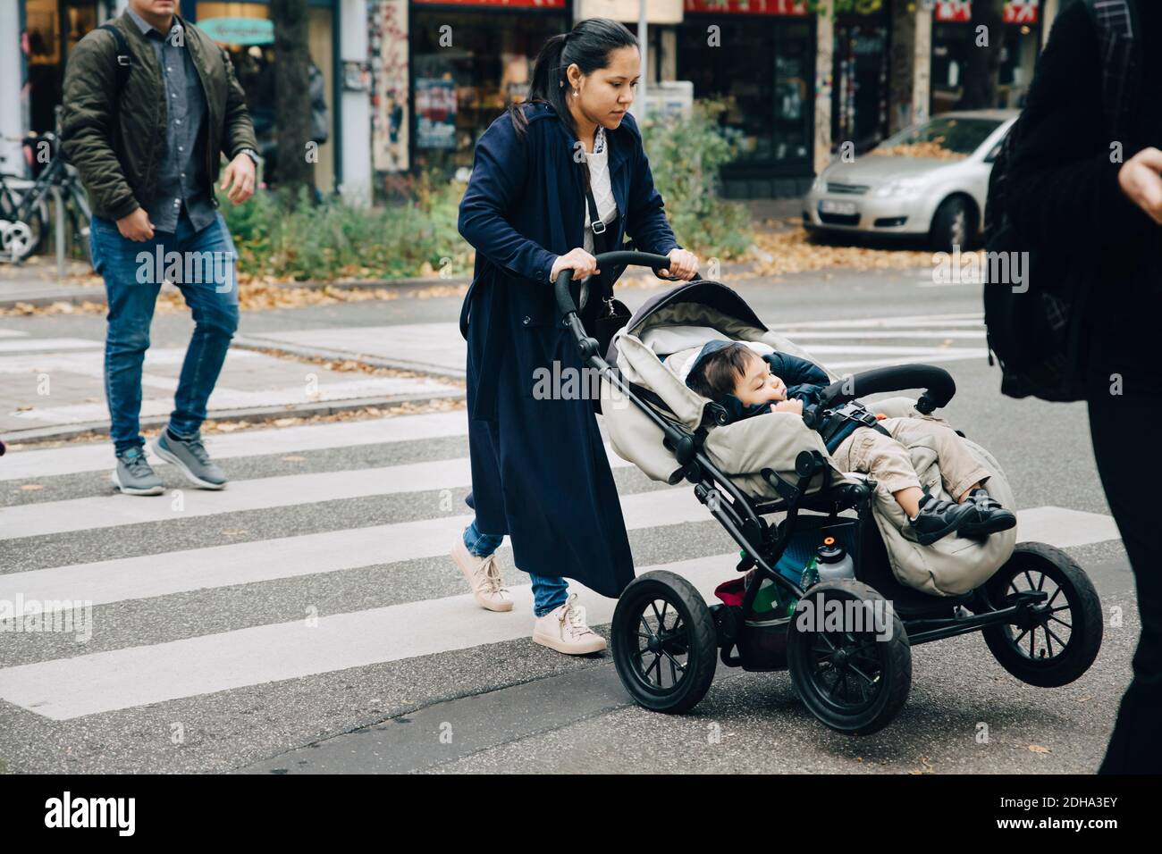 Full length of mother with son sitting in stroller crossing road in city Stock Photo
