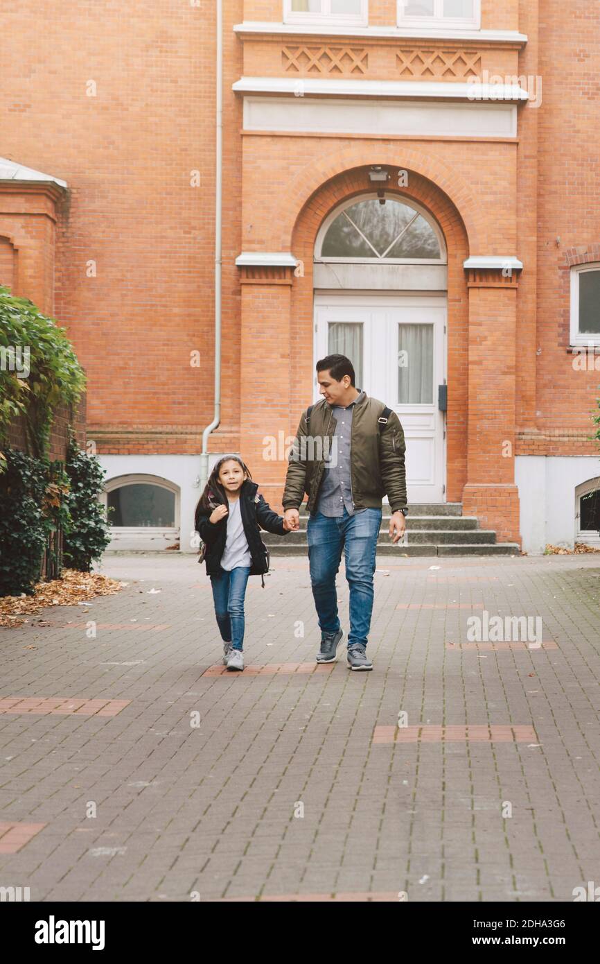 Full length of father and daughter walking home from school in city Stock Photo