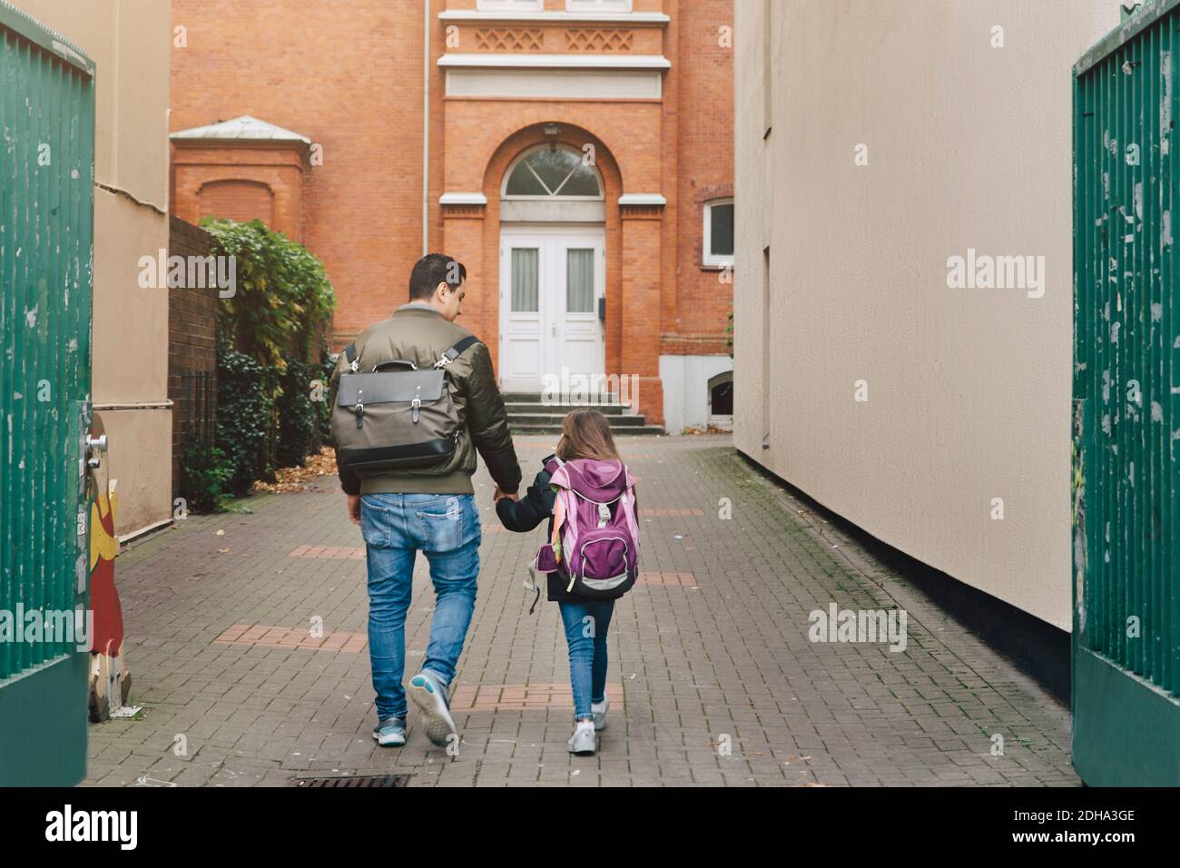 Rear view of father and daughter with backpack walking towards school Stock Photo