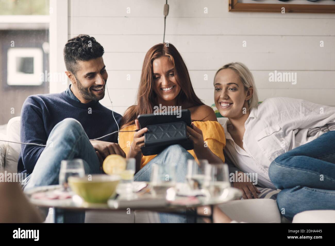 Cheerful young friends sharing digital tablet while sitting on sofa at home Stock Photo