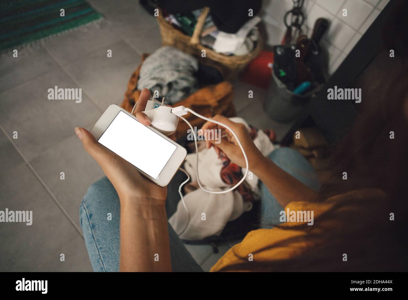 Midsection of young woman holding mobile phone and charger at home Stock Photo