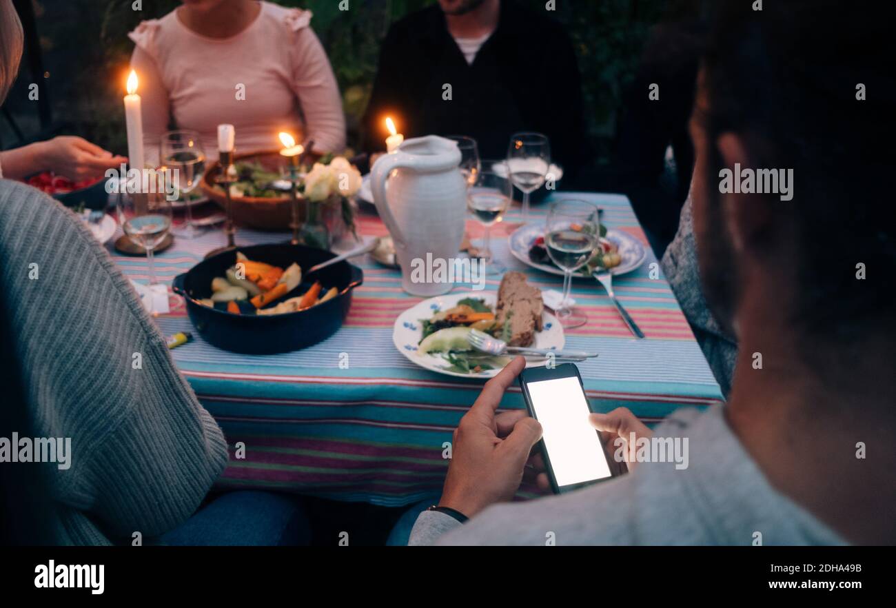 Cropped image of young man using smart phone while having dinner with friends Stock Photo