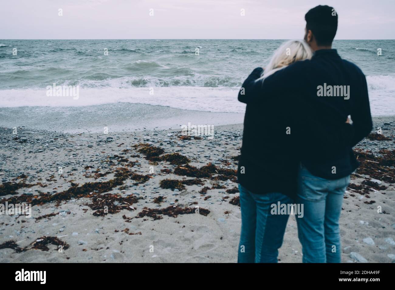Rear view of young couple standing on shore at beach Stock Photo