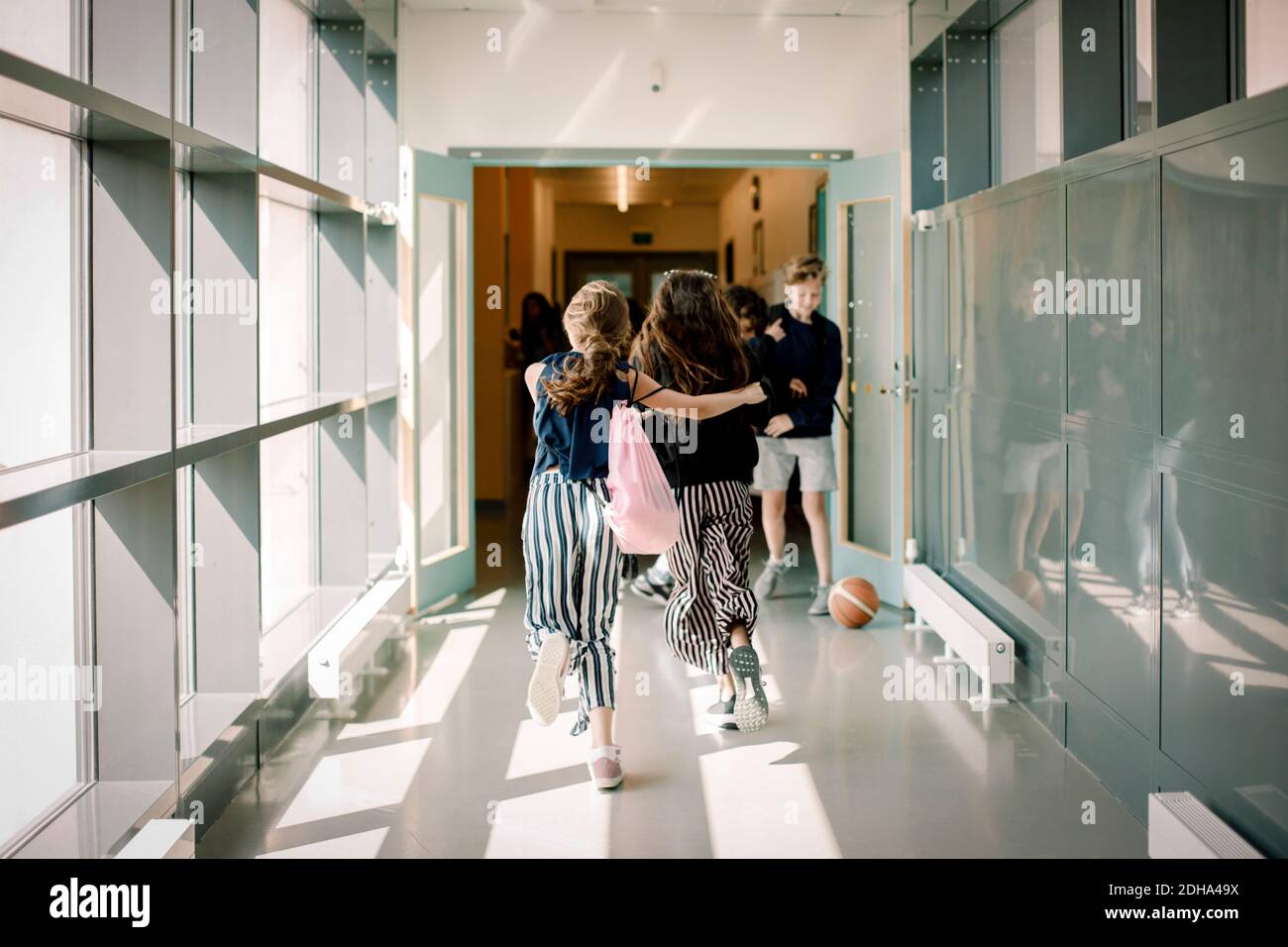 Rear view of female friends running in school corridor Stock Photo