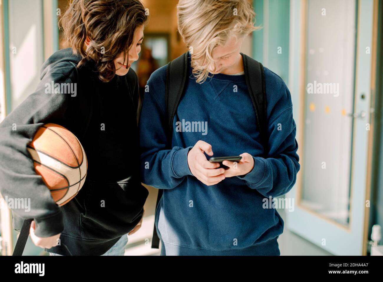 Male students using smart phone in school corridor Stock Photo