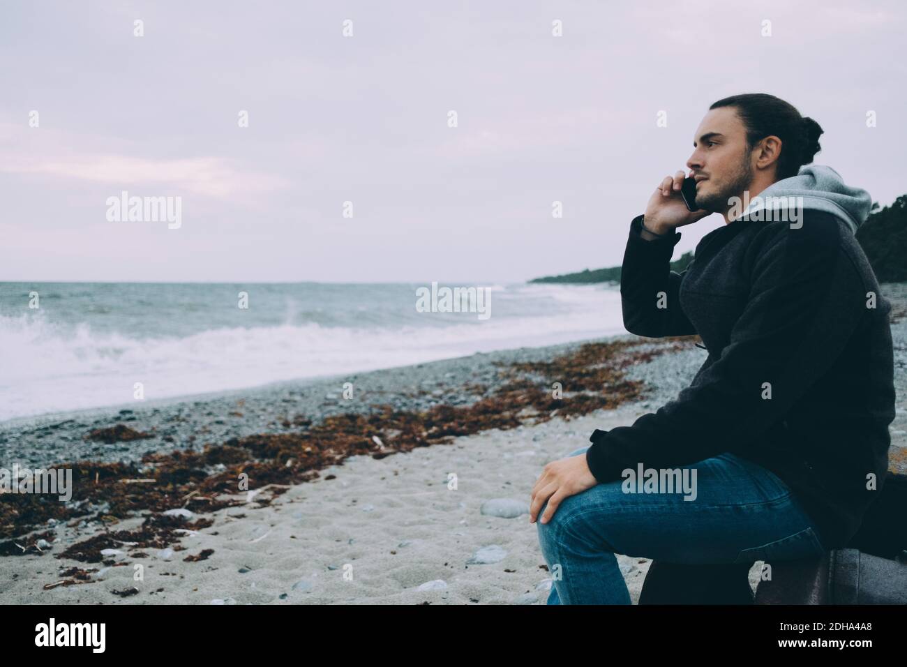 Side view of young man using mobile phone while sitting at beach Stock Photo