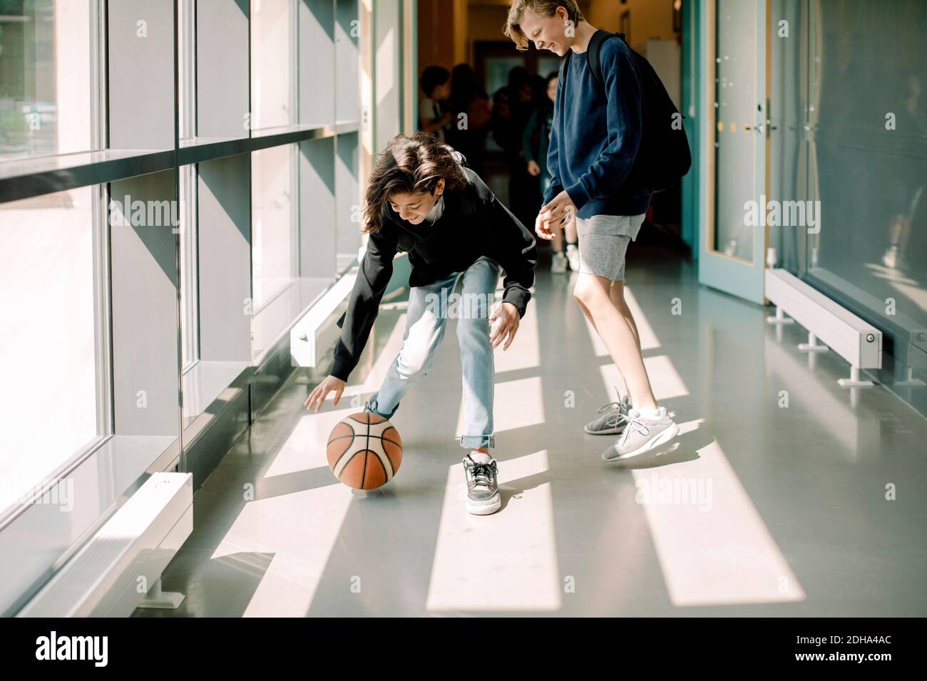 Smiling male students playing with basketball in school corridor Stock Photo