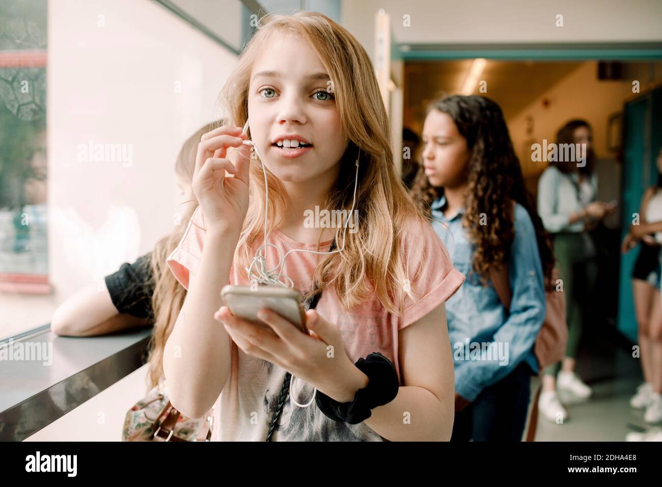 Female student talking through in-ear headphones in school corridor Stock Photo