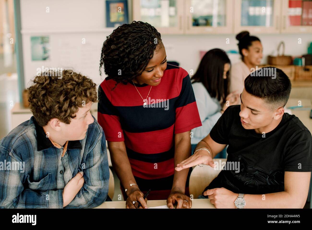 Male student gesturing while discussing with female teacher in classroom Stock Photo