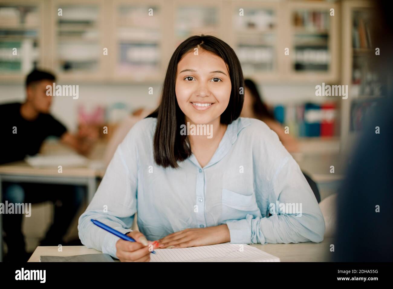 Portrait of smiling teenage girl studying at table in classroom Stock ...