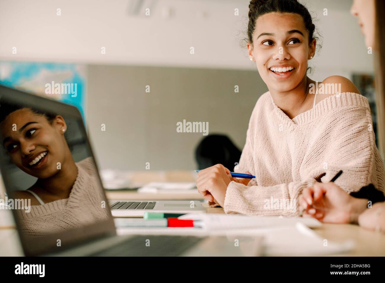 Smiling teenager studying with friend while sitting by table in classroom Stock Photo