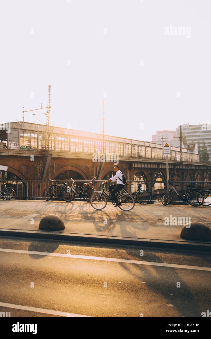 Full length of male entrepreneur riding bicycle on street in city against sky Stock Photo