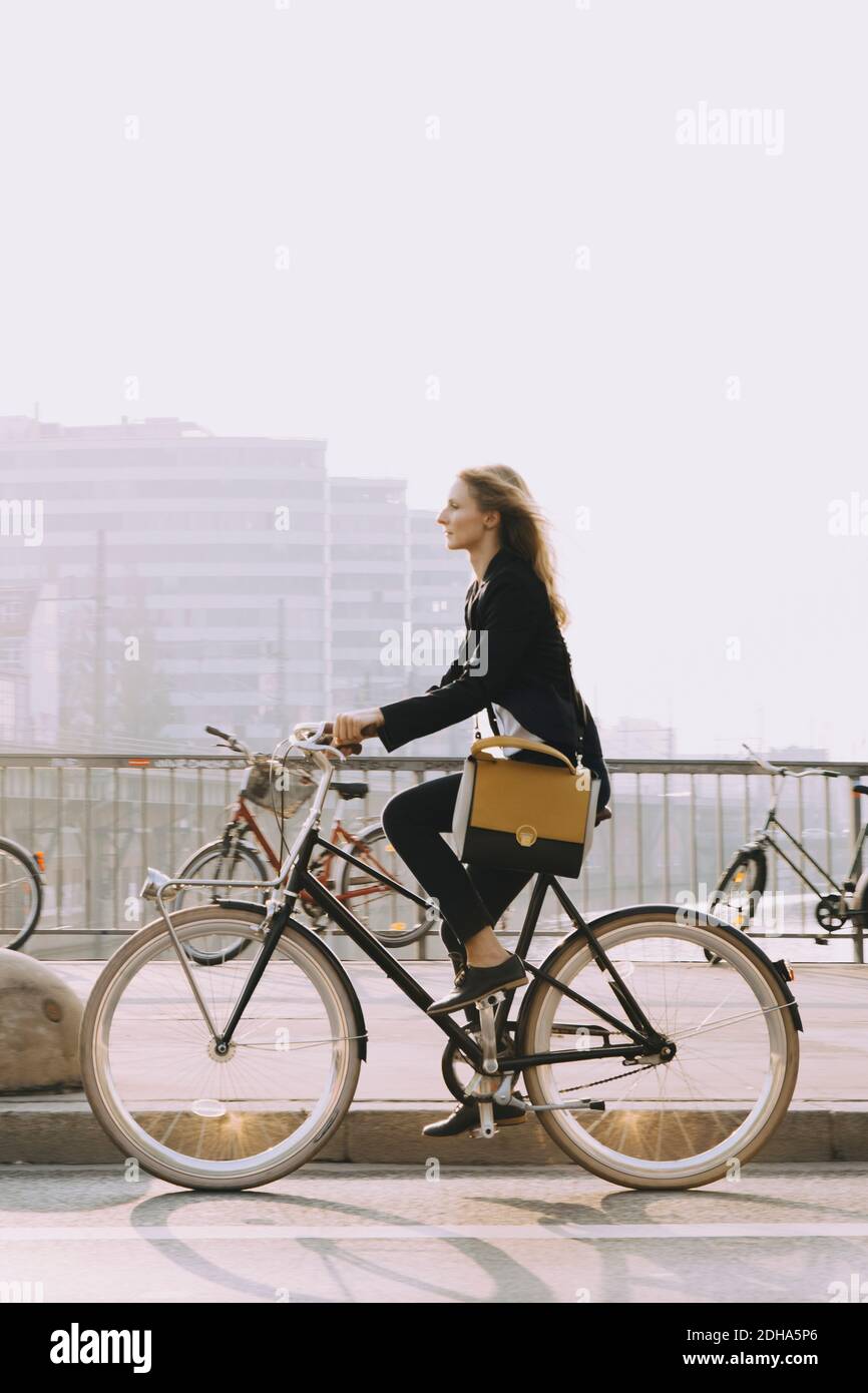 Side view of young businesswoman riding bicycle on street in city Stock Photo
