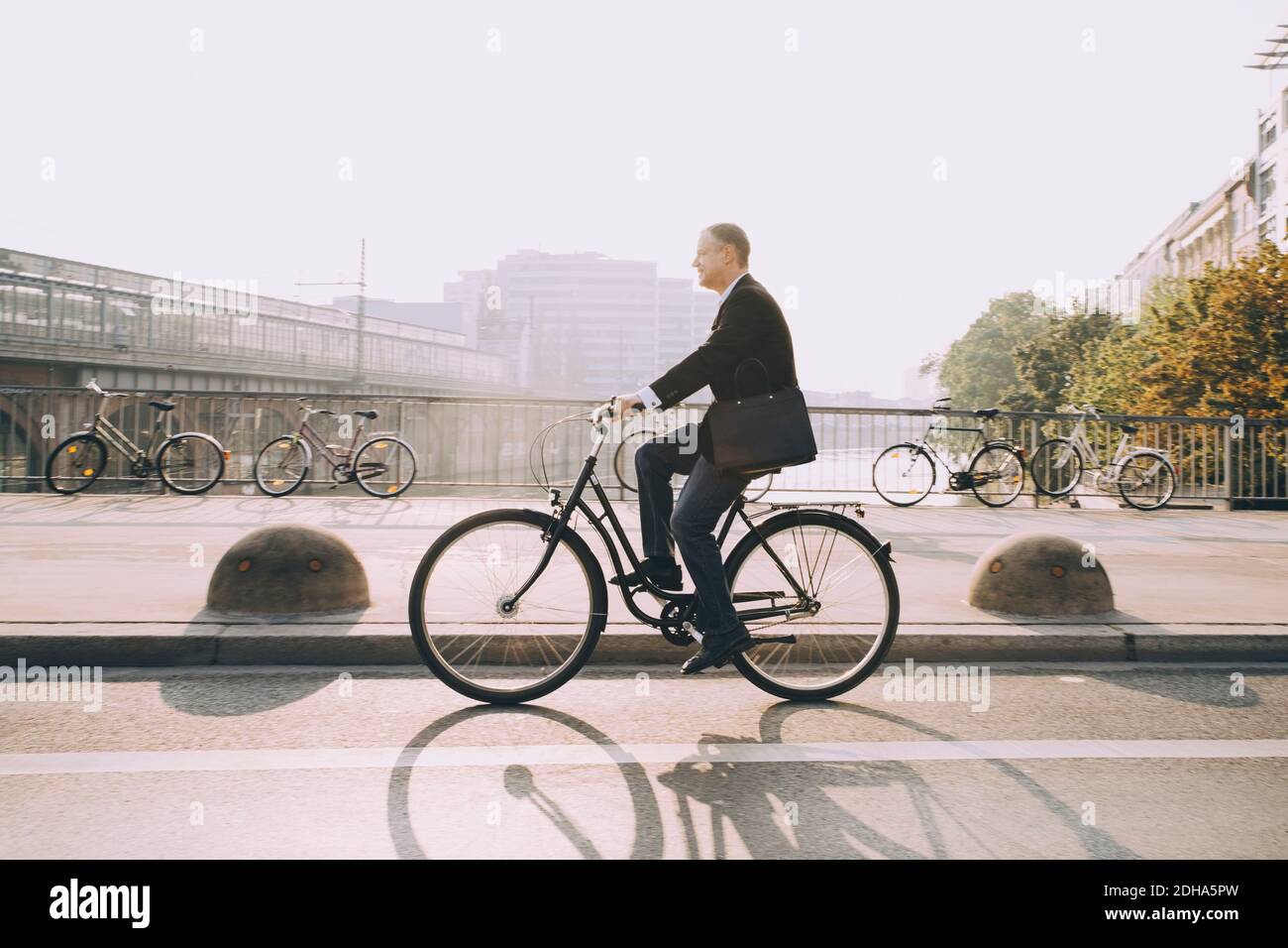 Side view of businessman riding bicycle on road in city against sky Stock Photo