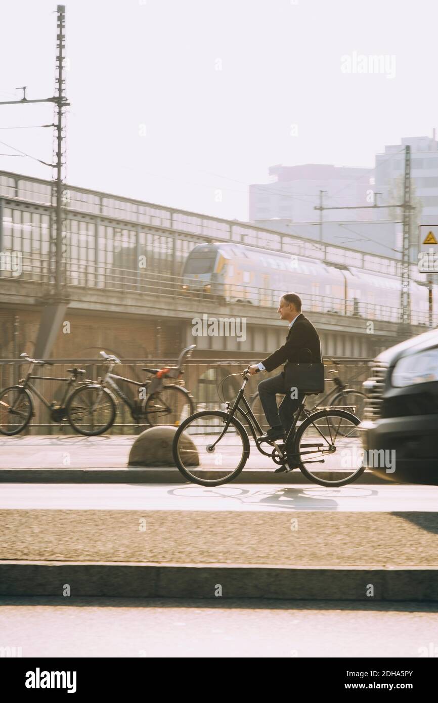 Male entrepreneur riding bicycle on road in city against sky Stock Photo