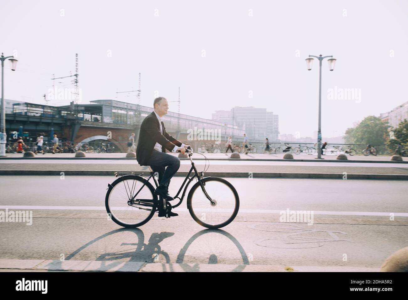 Side view of male entrepreneur riding bicycle on city street against sky Stock Photo